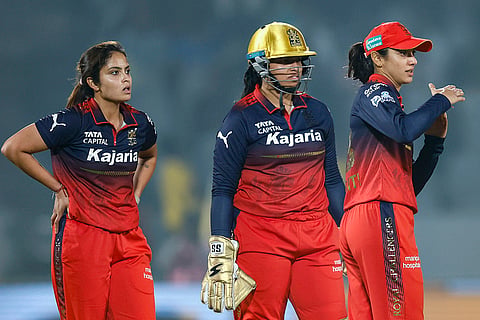 Royal Challengers Bengaluru’s Sayali Satghare, left, and Richa Ghosh, centre, look on as captain Smriti Mandhana takes an unsuccessful DRS review for the wicket of UP Warriorz’ captain Meg Lanning during a Women's Premier League (WPL) 2026 T20 International cricket match between Royal Challengers Bengaluru and UP Warriorz, at BCA Stadium, in Vadodara, Gujarat. 