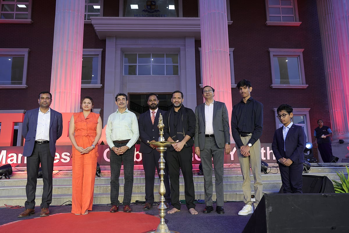 A group of individuals in formal attire standing on a stage in front of Manchester Global School