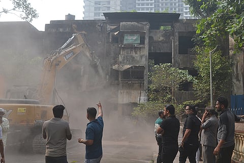 People look on as an excavator is used to demolish a dilapidated building, in Navi Mumbai.