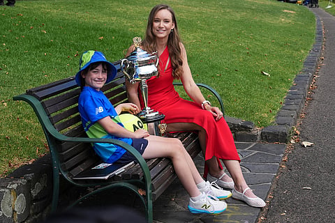 Elena Rybakina of Kazakhstan sits with ballkid Gladys Jarry as she poses with Daphne Akhurst Memorial Cup on the banks of the Yarra River the morning after defeating Aryna Sabalenka of Belarus in the women's singles final at the Australian Open tennis championship in Melbourne, Australia.