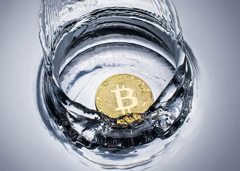 A gold Bitcoin coin splashing into clear water inside a glass container