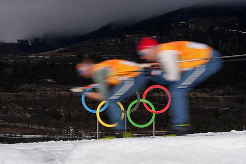 Athletes ski past Olympic rings during a cross country training session at the 2026 Winter Olympics, in Tesero, Italy.