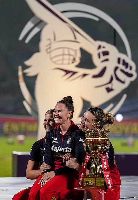 Royal Challengers Bengaluru's players pose with the trophy after winning the Women's Premier League (WPL) 2026 final T20 cricket match against Delhi Capitals, at Baroda Cricket Association Stadium, Kotambi in Vadodara, Gujarat.