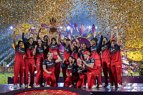 Royal Challengers Bengaluru's players celebrate with the trophy after winning the Women's Premier League (WPL) 2026 final T20 cricket match against Delhi Capitals, at Baroda Cricket Association Stadium, Kotambi in Vadodara, Gujarat