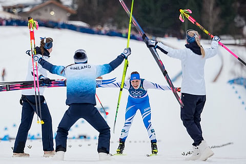 Jasmi Joensuu, of Finland, approaches the finish line and celebrating teammates to win the bronze medal in the cross country skiing women's 4 x 7.5km relay at the 2026 Winter Olympics, in Tesero, Italy.