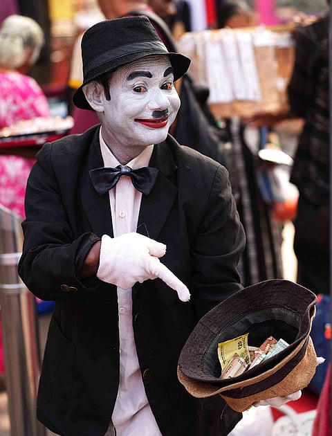 With a knowing smile, Afsar Khan—dressed as Charlie Chaplin—points to his hat as coins and notes collect inside, each contribution a small reward for the laughter he brings to the busy lanes of Dadar in Mumbai.