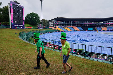 Iris fans walk by the covered ground as rain delayed the start of play during the T20 World Cup cricket match between Ireland and Zimbabwe in Pallekele, Sri Lanka.