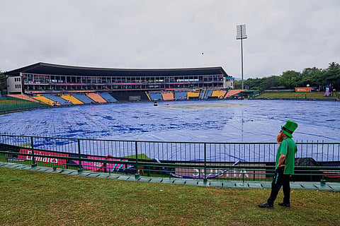 An Iris fan watches the covered ground as rain delayed the start of play during the T20 World Cup cricket match between Ireland and Zimbabwe in Pallekele, Sri Lanka.