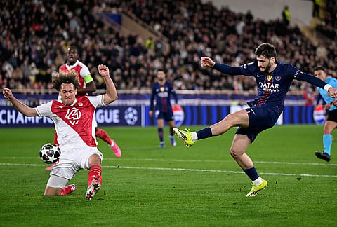 Monaco's Wout Faes, left, tries to block a shot from PSG's Khvicha Kvaratskhelia during the first-leg of the Champions League playoff soccer match between Monaco and Paris Saint-Germain in Monaco.