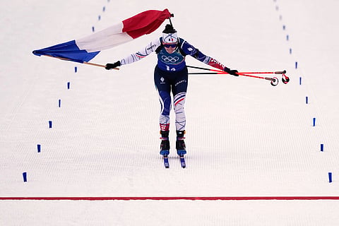 Julia Simon, of France, skis with her country's flag as she crosses the finish line for gold in the women's 4x6-kilometer relay biathlon race at the 2026 Winter Olympics in Anterselva, Italy.
