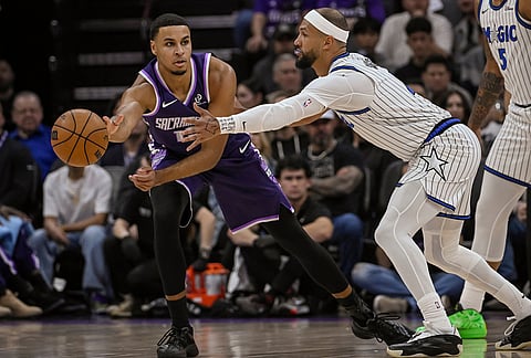Sacramento Kings forward Keegan Murray, left, pass the ball around Orlando Magic guard Jalen Suggs, second from left, during the first half of an NBA basketball game in Sacramento, California.