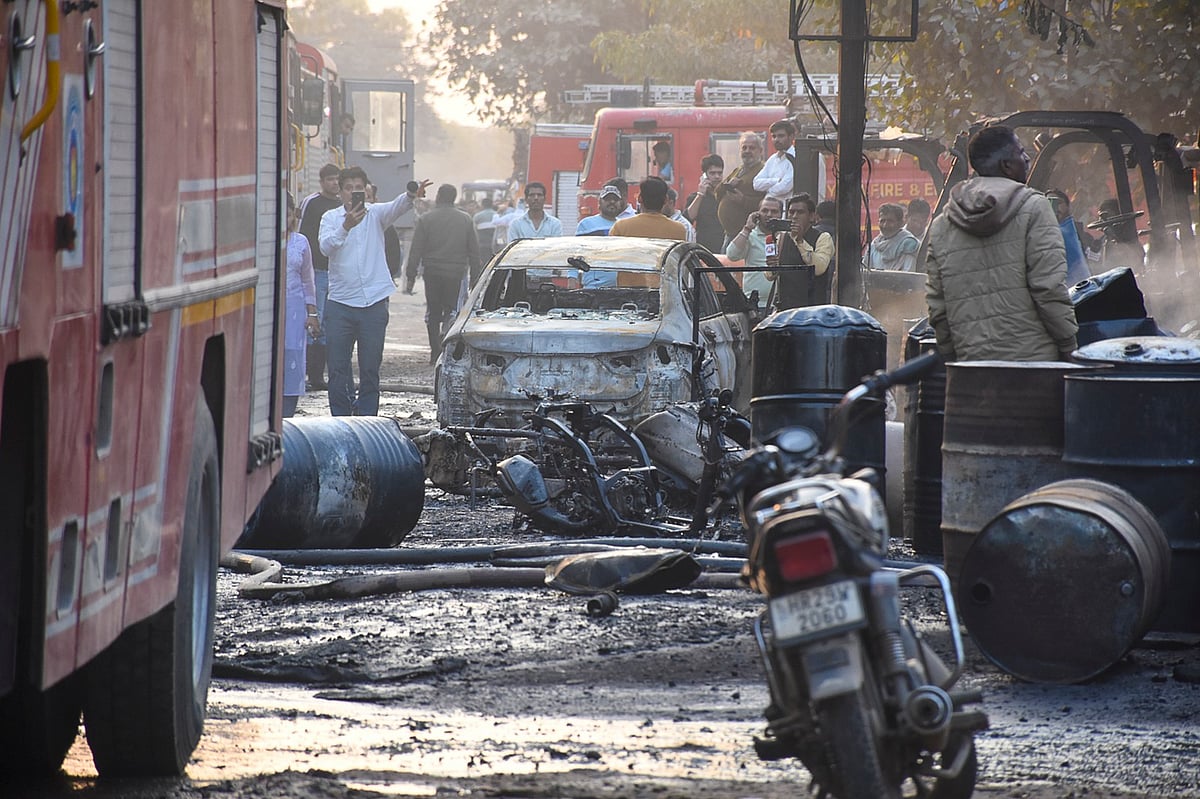 PTI : People gather around charred remains after a fire broke out at a factory in Sector 24, in Faridabad, Monday, Feb. 16, 2026. More than 35 people were rushed to hospitals with burns in the incident.