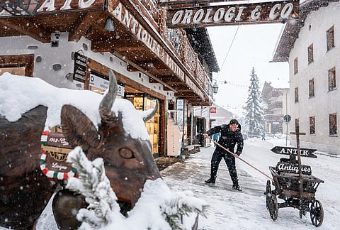 A person removes snow from a storefront during the 2026 Winter Olympics in Livigno, Italy. 