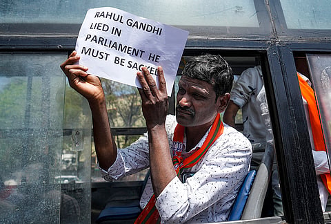 A Bharatiya Janata Yuva Morcha (BJYM) activist holds a placard as he is detained by Karnataka Police during a protest against Congress over Youth Congress workers' shirtless disruption at the AI Impact Summit, in Bengaluru.