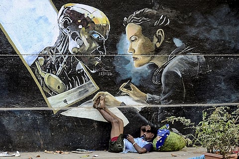 A man rests beneath a mural depicting an AI robot and a human face at Seawoods, in Navi Mumbai, Maharashtra.
