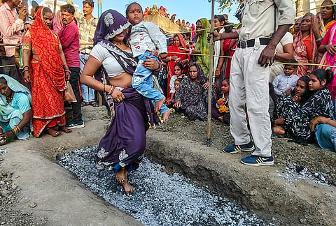 A woman carrying a child walks over burning embers during the 'Gal Chul' ritual held as part of Holi celebrations, at Khajuriya village near Indore, Madhya Pradesh.