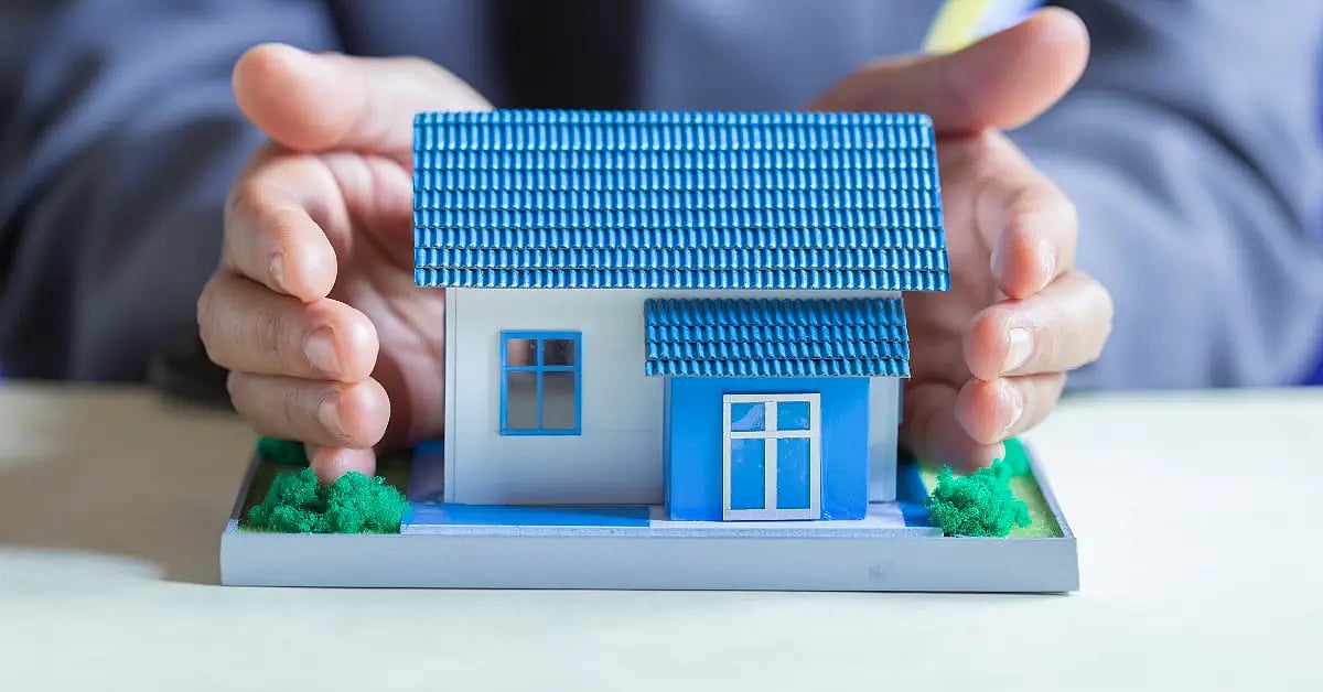 A man cupping a small model house, symbolizing homebuyer protection in real estate