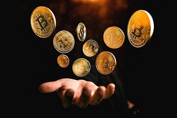 Floating cryptocurrency coins like Bitcoin above an open hand on a dark background.