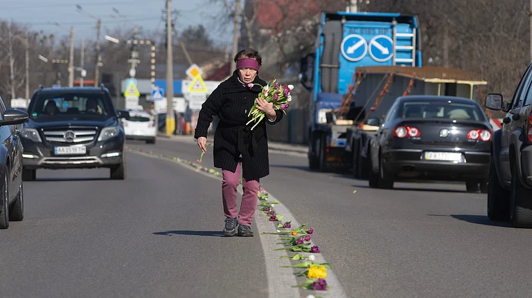 A villager lays flowers on a road in the village of Novi Petrivtsi close to capital Kyiv, Ukraine, Thursday, March 12, 2026, ahead of a funeral procession for a Ukrainian army soldier who was killed in a battle with Russian troops. - Credit: AP Photo/Efrem Lukatsky