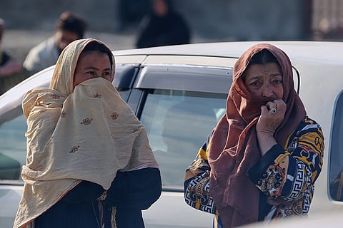Two women watch as rescue workers and officials inspect the site of a late-Monday airstrike at a drug rehabilitation hospital in Kabul, Afghanistan.