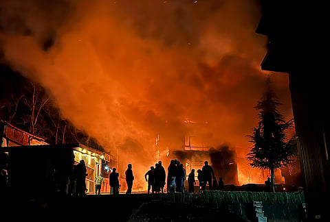 People gather as flames and smoke rise from hotel structures following a fire, in Pahalgam, Anantnag district, Jammu and Kashmir.