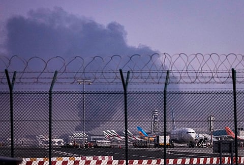Planes are parked at Dubai International Airport as smoke rises in the background after a drone struck a fuel tank early morning, forcing the temporary suspension of flights, in Dubai, United Arab Emirates.