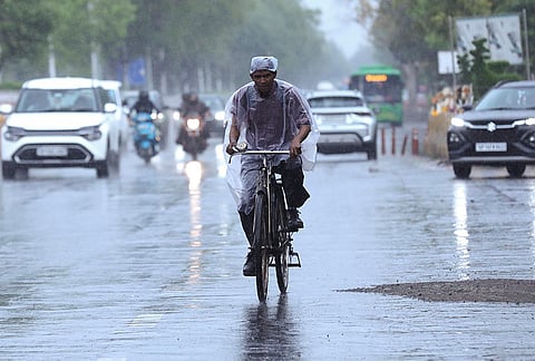 A man covers himself with a plastic sheet while pedaling a bicycle amid rain, in Noida.