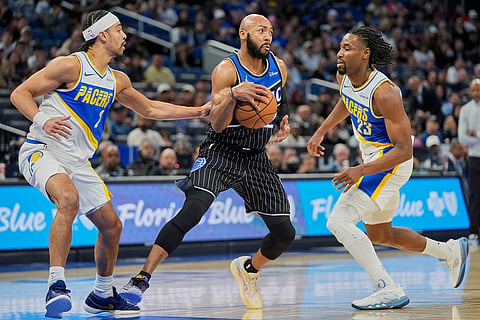 Orlando Magic guard Jevon Carter, center, makes a move to get through Indiana Pacers forward Obi Toppin, left, and guard Aaron Nesmith (23) during the first half of an NBA basketball game in Orlando, Fla.