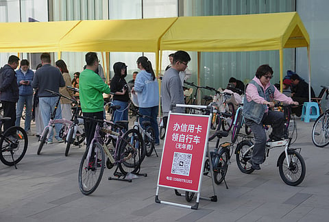A woman tries out a bicycle as people seek information about a credit card application at a booth set up outside an office building in Beijing, China. The signboard reads, "Get a bicycle by applying for a credit card with no annual fees." 