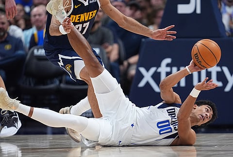 Dallas Mavericks guard Max Christie passes the ball as he falls on the court in the second half of an NBA basketball game against the Denver Nuggets in Denver.