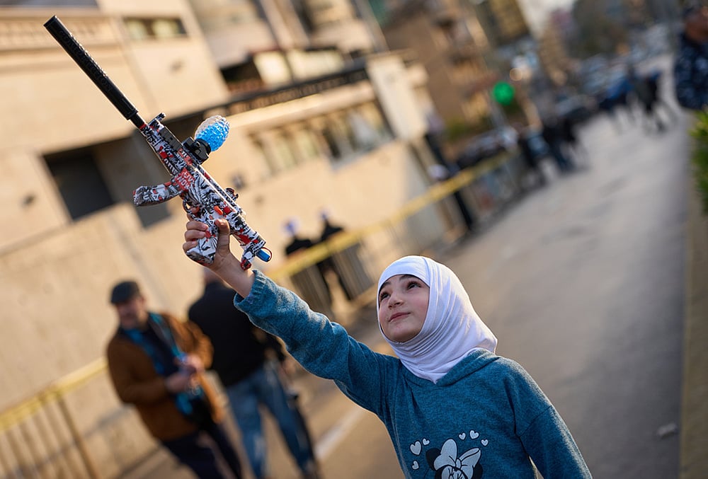 A girl holds a toy gun during a protest outside Iran's embassy, where dozens of people gathered waving Hezbollah and Iranian flags in solidarity with the Islamic Republic, in Beirut, Lebanon. - | Photo: AP/Emilio Morenatti