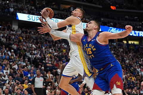 Golden State Warriors forward Kristaps Porziņģis, left, is fouled as he drives to the rim past Denver Nuggets center Nikola Jokić in the second half of an NBA basketball game in Denver.