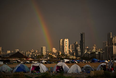 Displaced people who fled Israeli strikes in southern Lebanon sit inside tents used as shelters as a rainbow breaks through the rain in Beirut, Lebanon.