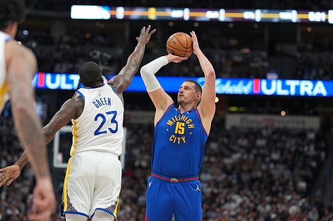 Denver Nuggets center Nikola Jokić, right, goes up for. basket as Golden State Warriors forward Draymond Green defends in the first half of an NBA basketball game in Denver. 