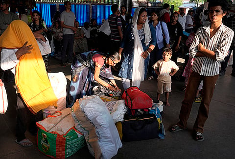 Passengers wait with their luggage at the platform, checking and rearranging their belongings as they prepare for departure.