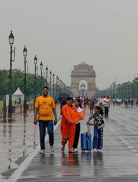 Visitors walk along a rain-soaked road amid rainfall, at India Gate, in New Delhi.