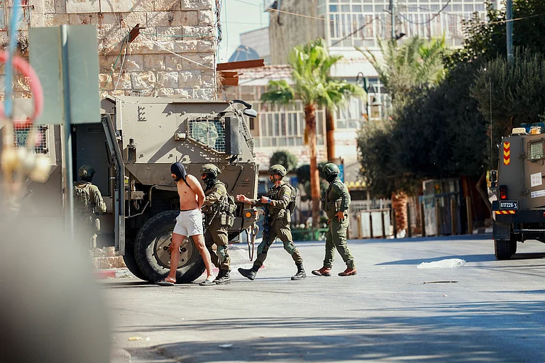 Israeli Raid In Al Birah West Bank Israeli soldiers escort a detained man near a military vehicle in Al Birah, West Bank on October 7, 2025 - Credit: IMAGO / Middle East Images