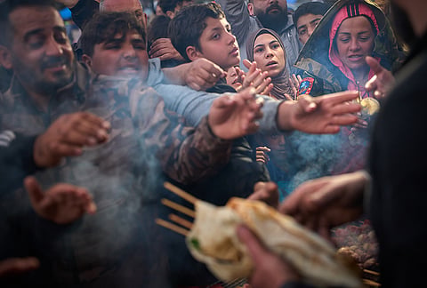 Displaced families extend their hands while waiting for donated food beside the tents they use as shelters after fleeing Israeli bombardment in southern Lebanon, in Beirut, Lebanon, Thursday, April 9, 2026. 