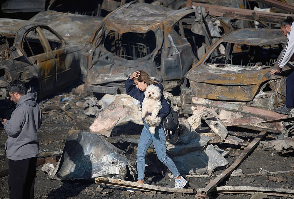 A woman holds her dog as she walks past burned cars a day after an Israeli airstrike in Beirut, Lebanon, Thursday, April 9, 2026.  - | Photo: AP/Emilio Morenatti
