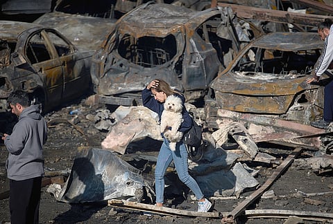A woman holds her dog as she walks past burned cars a day after an Israeli airstrike in Beirut, Lebanon, Thursday, April 9, 2026. 
