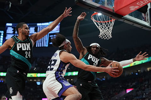 Sacramento Kings guard Devin Carter (22) tries to pass the ball around Portland Trail Blazers forward Kris Murray (24) and center/forward Robert Williams III (35) during the first half of an NBA basketball game in Portland, Ore.