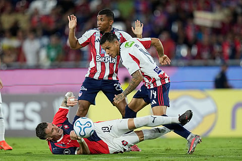 Pablo Vegetti of Paraguay's Cerro Porteño, on the ground, falls as he vies for the ball with Juan Rios of Colombia's Junior, right, during a Copa Libertadores Group F soccer match soccer match in Asuncion, Paraguay.