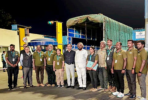 In this image posted on April 18, 2026, officials pose for a group photograph near a transport vehicle used for shifting cheetahs after their arrival in the city, in Bengaluru. 