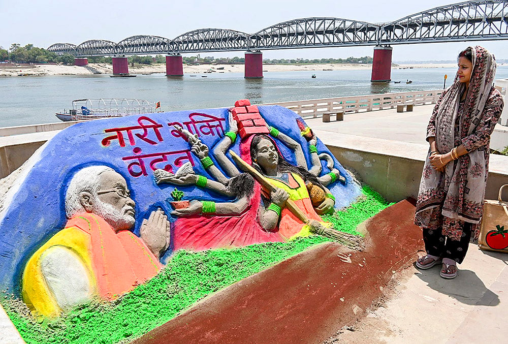 | Photo: PTI : A woman looks at a sand art carved by Sand artist Rupesh Singh dedicated on 'Nari Shakti Vandan Adhiniyam', commonly known as Women's Reservation Act, at Namo Ghat, in Varanasi, Uttar Pradesh.