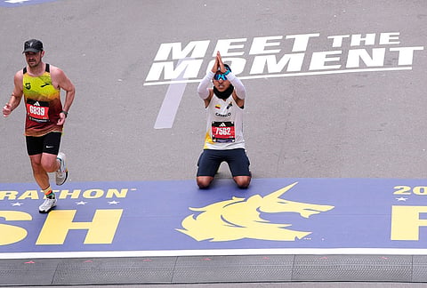 Runner Camilo Cubillos, of Colombia, kneels on the finish line after completing the Boston Marathon, in Boston.