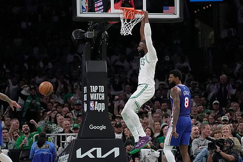 Boston Celtics guard Jaylen Brown, top, hangs from the rim after dunking against Philadelphia 76ers forward Paul George (8) during the second half in Game 1 of a first-round NBA playoffs basketball game in Boston.