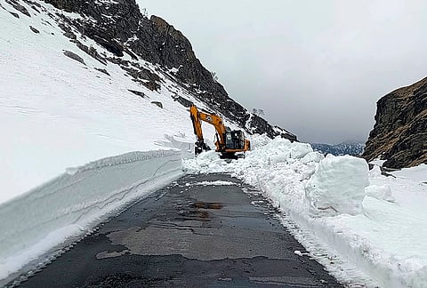 BRO personnel remove snow blocking a road through an excavator, at Rohtang Pass, in Kullu district, Himachal Pradesh.