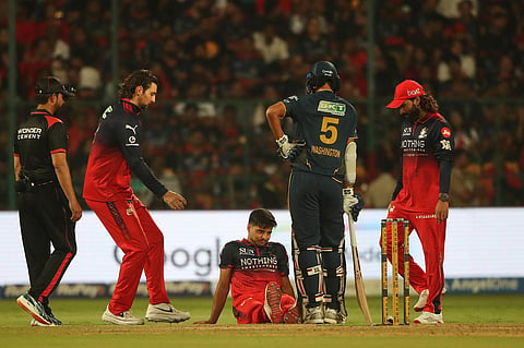 Royal Challengers Bengaluru's Rasikh Dar sits on the ground after getting injured during the Indian Premier League cricket match between Royal Challengers Bengaluru and Gujarat Titans in Bengaluru.