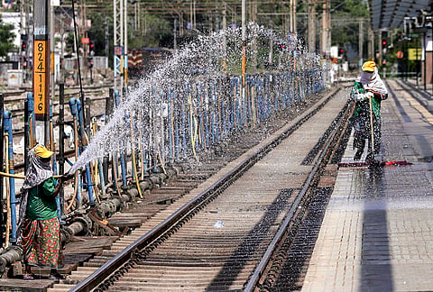 A railway worker sprinkles water on a platform amid scorching heat at Prayagraj Junction railway station, in Prayagraj.