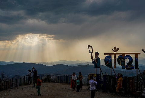 People gather at a viewpoint as clouds hover and sun rays pierce through them, in Shimla, Himachal Pradesh..